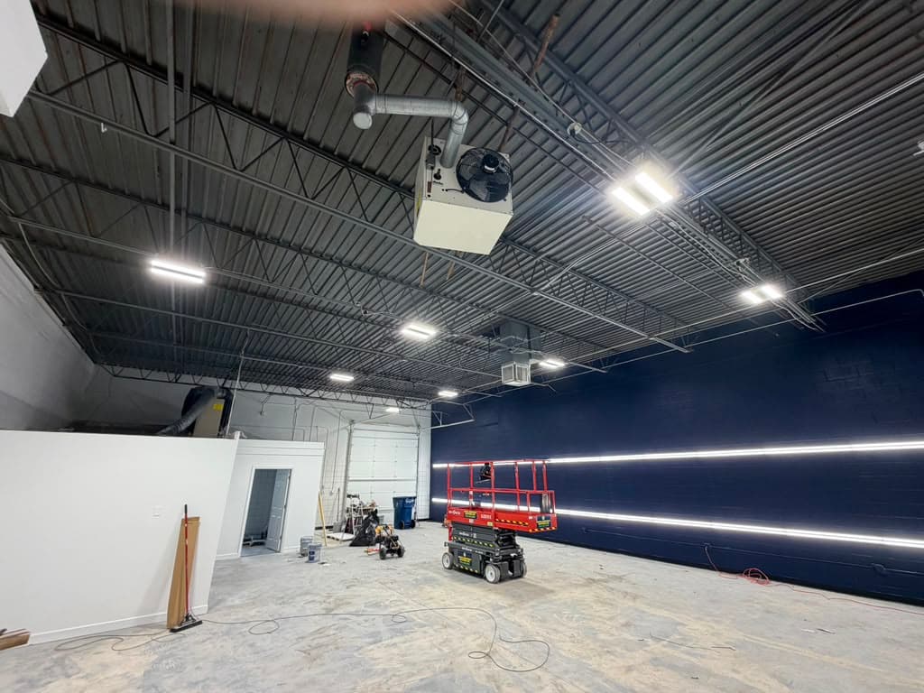 Red scissor lift in a warehouse with bright ceiling lights and a dark blue wall.
