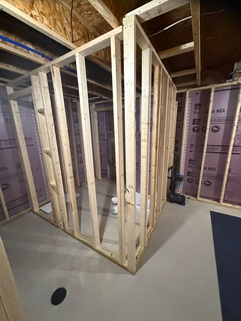 Interior wooden wall framing for a small basement room with purple rigid foam insulation.