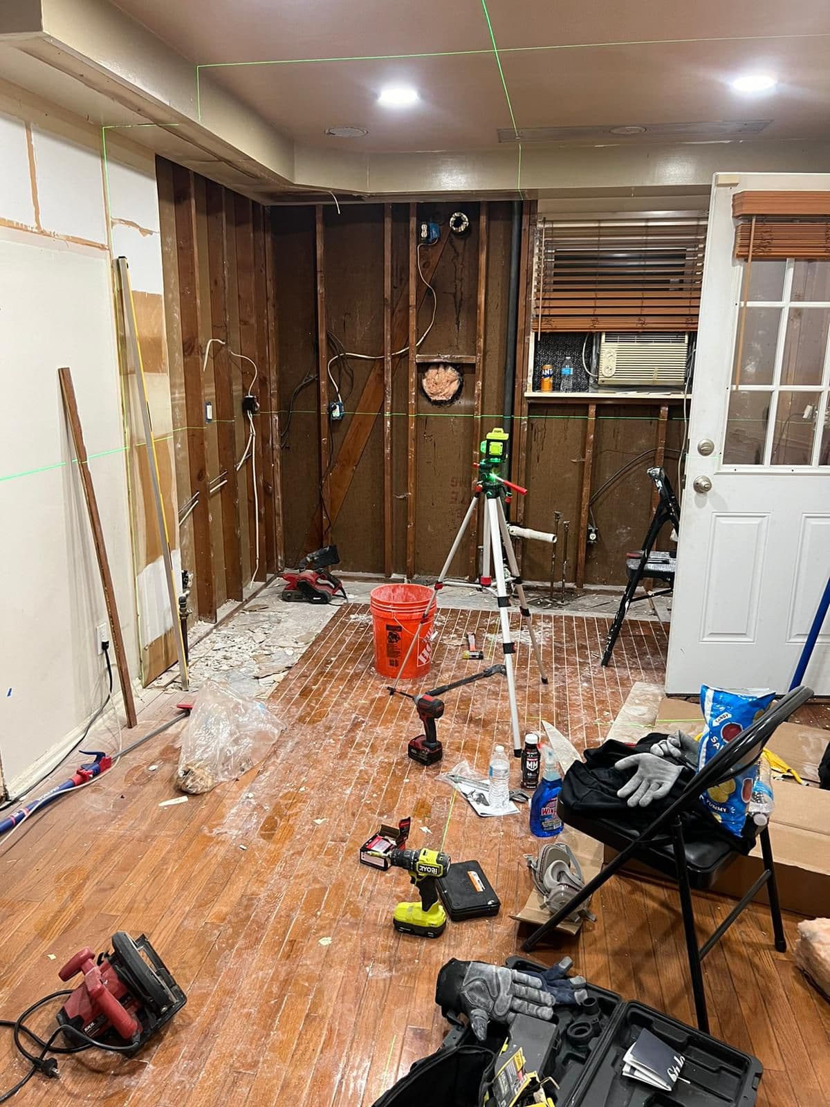 Room renovation with exposed wall studs, a green laser level, and scattered construction tools.