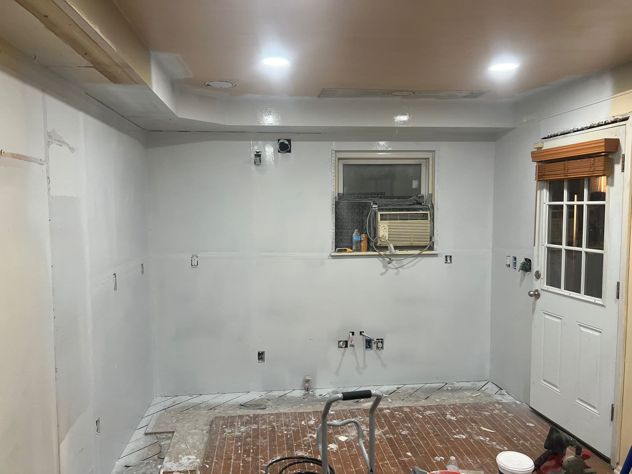 Interior room under renovation with white walls, exposed plumbing, electrical outlets, and tiled flooring.